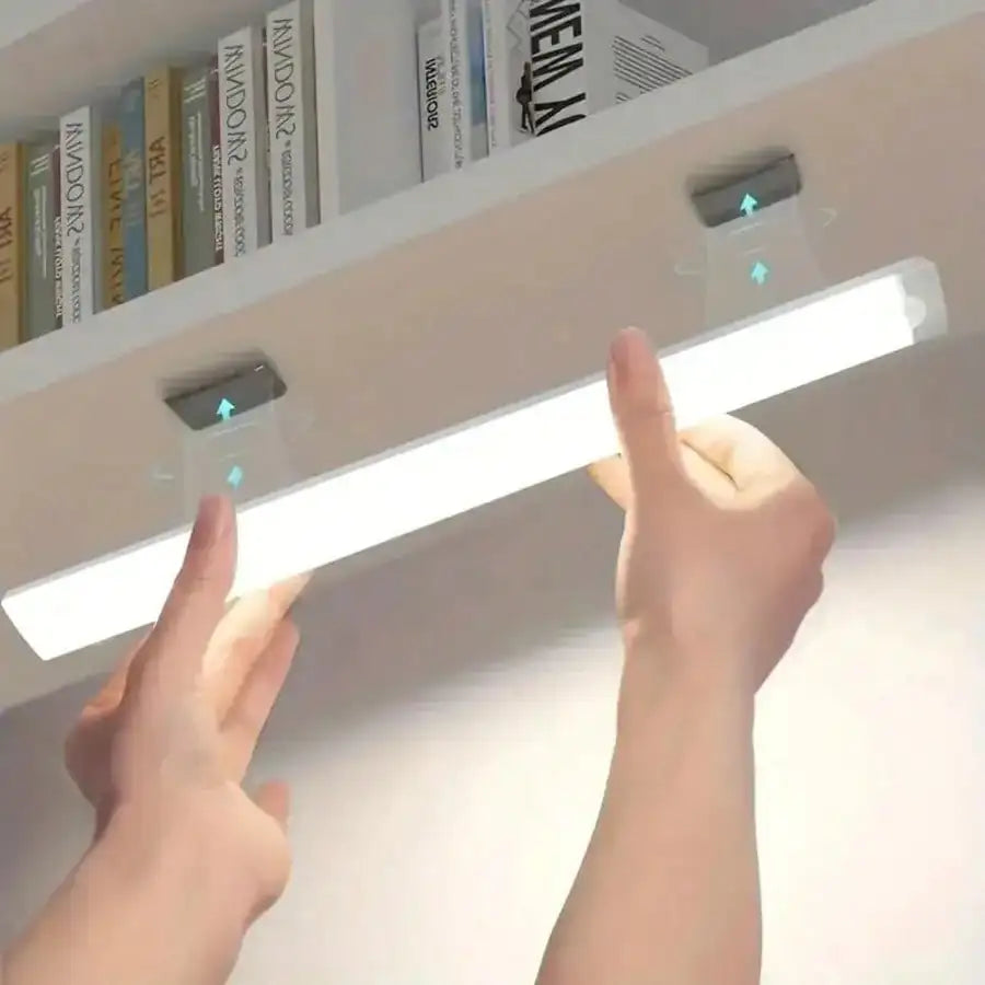 Hands are adjusting a white LED light bar with motion sensors mounted on a shelf.