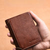 A hand holds a brown slim PU leather card holder wallet for men against a light orange background.