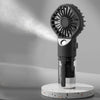 A black portable USB rechargeable mist fan with a circular grille and a clear glass container sits on a speckled white base.