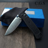 A black ultralight EDC folding knife with a drop point blade is shown resting on a blue box.