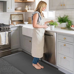 A woman stands on a gray anti-fatigue standing mat in a kitchen, preparing to cook.