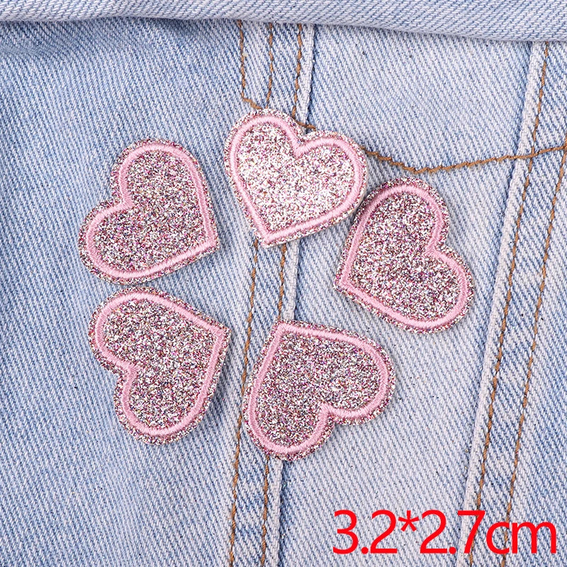 A set of five pink glitter heart iron-on embroidered patches placed on a light blue denim fabric.
