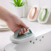 A hand is holding a green magic sponge scrubber with a long handle over a white sink.