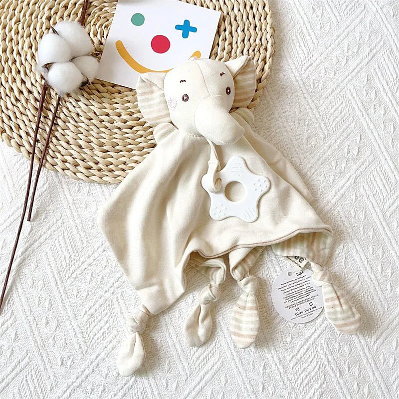 A cream-colored elephant plush toy with a teether, rattle, and comfort blanket resting on a woven mat.