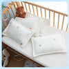 A stack of white quilted baby pillows with small gold star embroidery resting on a wooden crib railing.