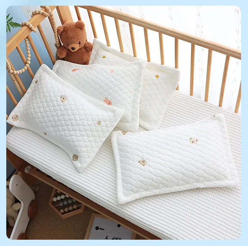A stack of white quilted baby pillows with small gold star embroidery resting on a wooden crib railing.