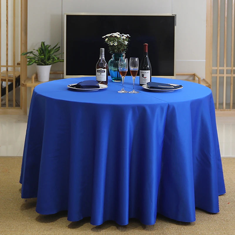 A round table set with a blue satin tablecloth, wine glasses, and bottles on a dark background.