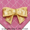A set of five gold and bronze sequin bow patches for DIY crafts displayed on a pink grid background.