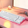 A pink acrylic ergonomic keyboard riser with a non-slip base is placed on a desk next to a computer monitor and a candle.