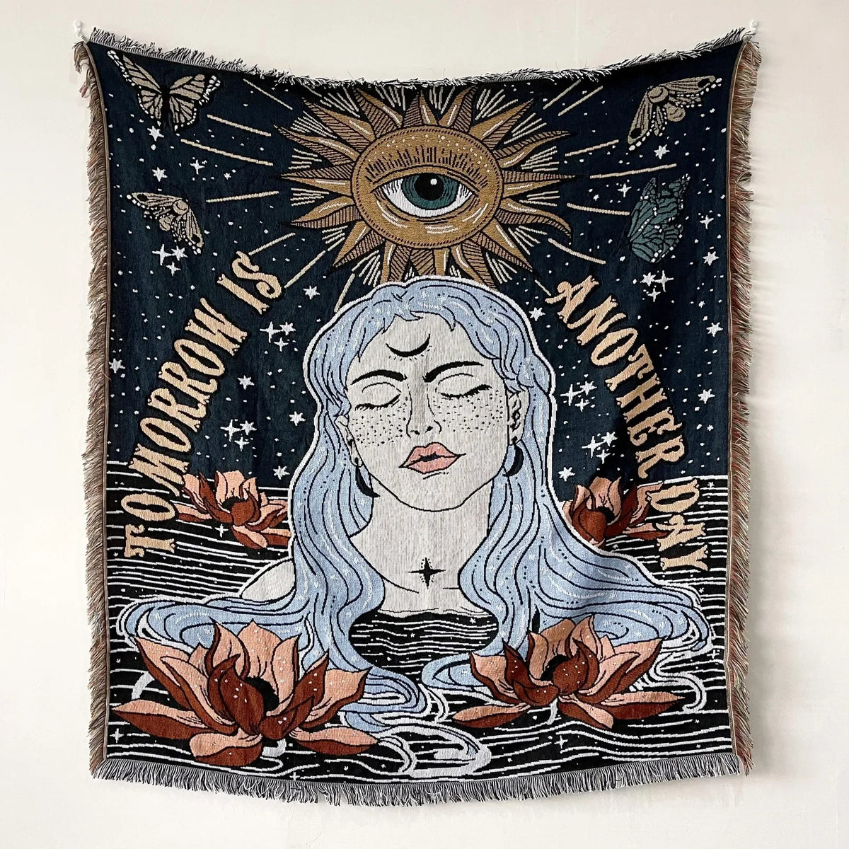 A dark tapestry featuring a face surrounded by sun rays and leaves with the text Tomorrow is another day