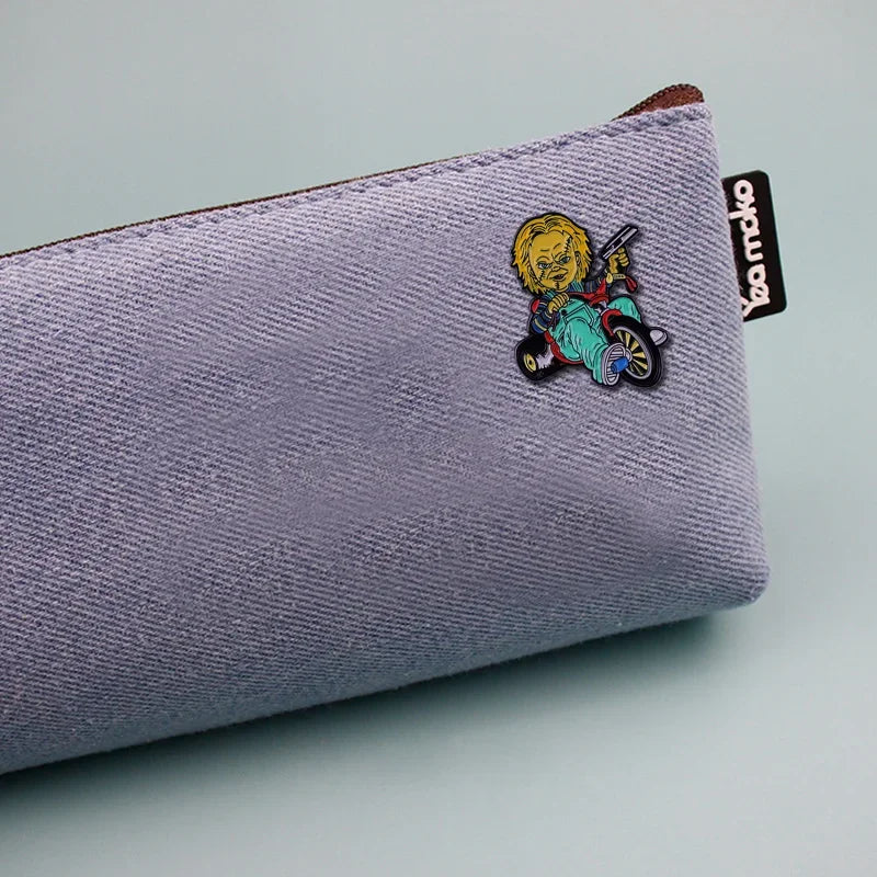 A purple fabric pouch with a yellow Chucky horror movie enamel pin brooch attached to the side.
