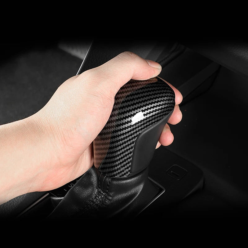 A hand is gripping a carbon fiber gear shift knob cover for a Toyota Camry or Corolla.