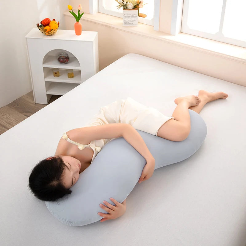 Una persona está tumbada en una cama blanca usando una almohada lateral ergonómica curva en forma de ola azul claro.