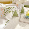 White lightweight summer comforter with a green and orange leaf print and lace trim resting on a white quilted surface.