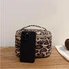 A black smartphone is placed on top of a leopard print cosmetic bag with a gold zipper on a wooden surface.