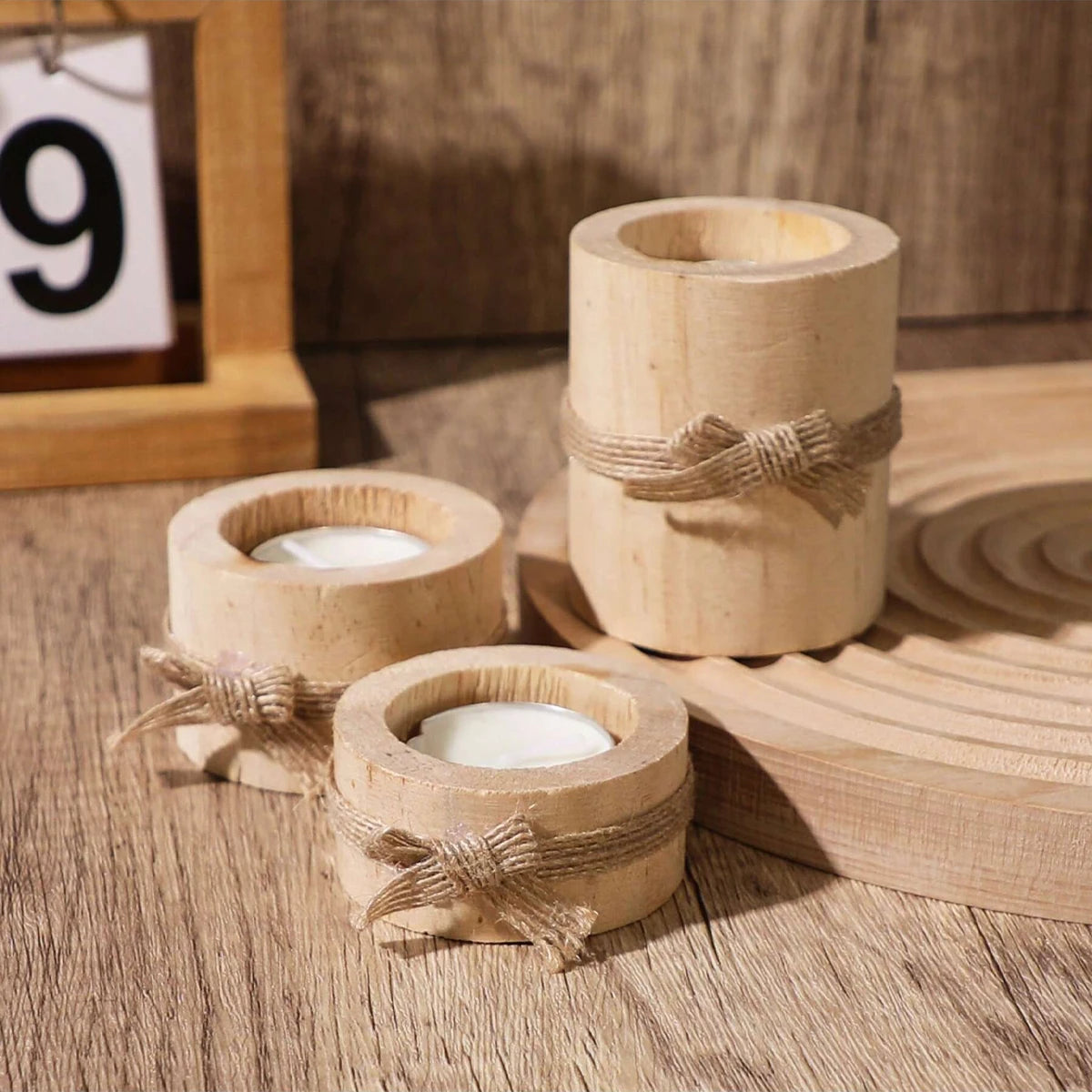 Three rustic wooden tea light holders with natural twine tied around the base resting on a wooden surface.