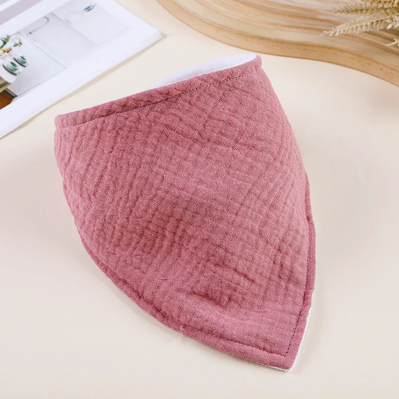 A pink, quilted soft cotton baby bib is shown on a light surface.