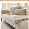 A beige chenille sofa cover with gray pillows and a protective layer on a bed.
