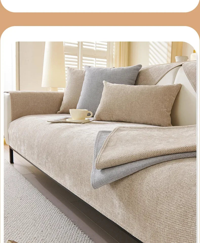 A beige chenille sofa cover with gray pillows and a protective layer on a bed.