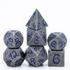 A set of seven metal polyhedral dice with a dragon font design stacked and displayed on a white background.