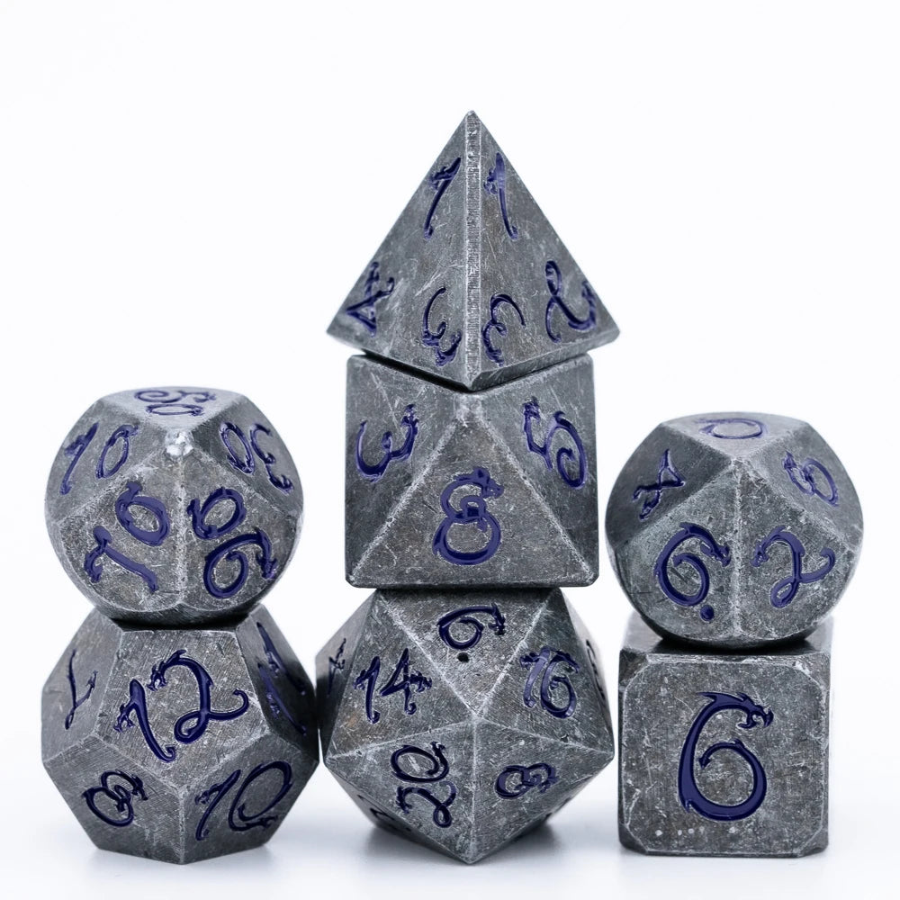A set of seven metal polyhedral dice with a dragon font design stacked and displayed on a white background.