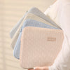 Una pila de fundas protectoras para laptops de color claro, con tonos beige y azul.