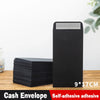 A black self-adhesive cash envelope is shown next to a stack of black envelopes on a wooden surface.