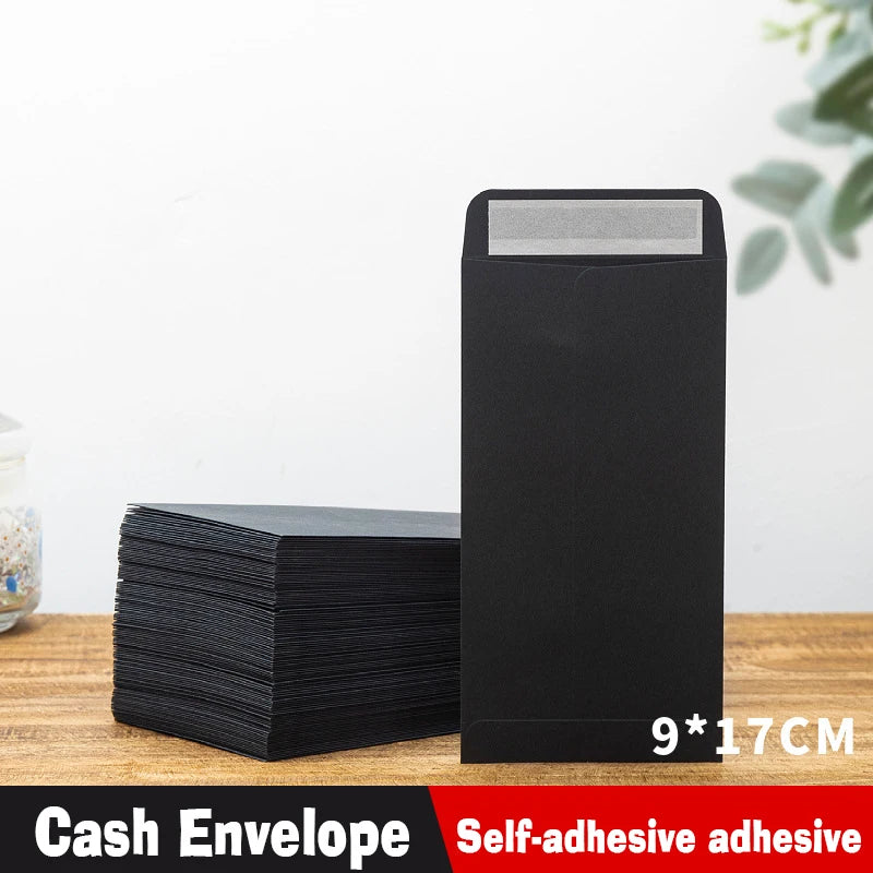 A black self-adhesive cash envelope is shown next to a stack of black envelopes on a wooden surface.