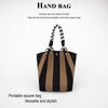 A black and tan striped square hand bag with a braided strap is shown against a white background.