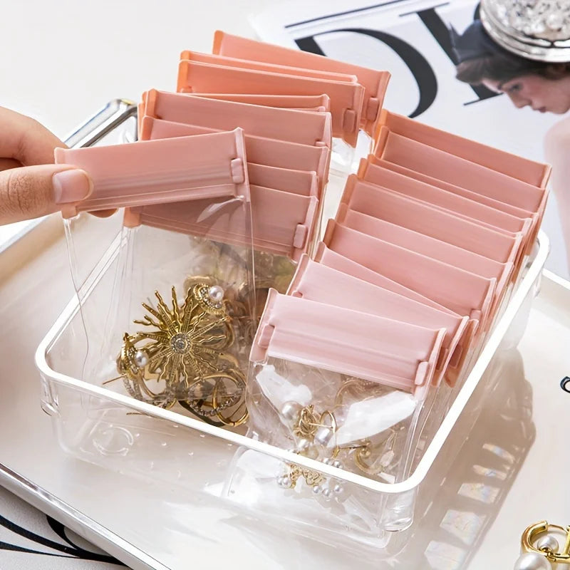 A clear storage box filled with 30 pink self-sealing EVA pouches for jewelry like rings, necklaces, and bracelets.