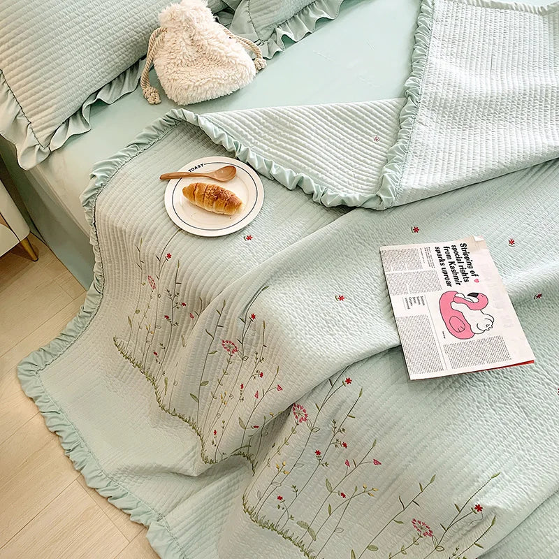 Light mint green quilted bedspread set with embroidered floral patterns and a fluffy cream pillow.