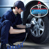 A man in a dark blue uniform is using a tool to work on a tire while a neon sign logo is visible in the background.