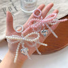 A hand holds a pink pearl bow keychain with heart charms against a light background.