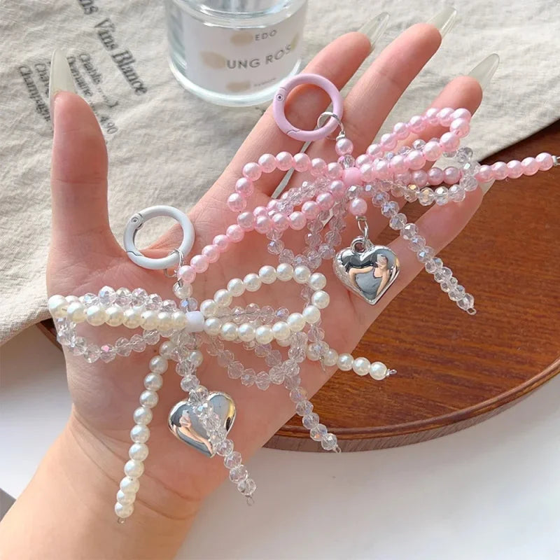 A hand holds a pink pearl bow keychain with heart charms against a light background.