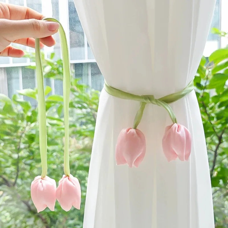 A hand holds a set of pink tulip curtain tie backs with green stems against a white fabric backdrop.