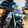 A person riding a motorcycle with a bright LED headlight and flames in the background.
