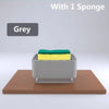A grey kitchen soap dispenser holding a green sponge on a wooden surface.