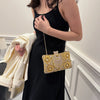 A woman wearing a black dress holds a gold rhinestone evening clutch with a chain strap.