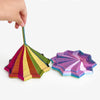 A hand holds a colorful 3D illusion fidget star toy with spiraling, iridescent plastic segments.