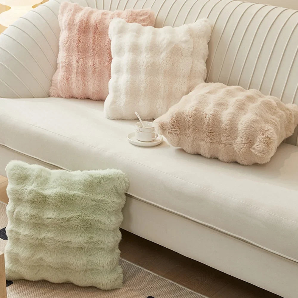 A collection of soft, fluffy decorative pillows in shades of pink, cream, and beige resting on a white sofa.