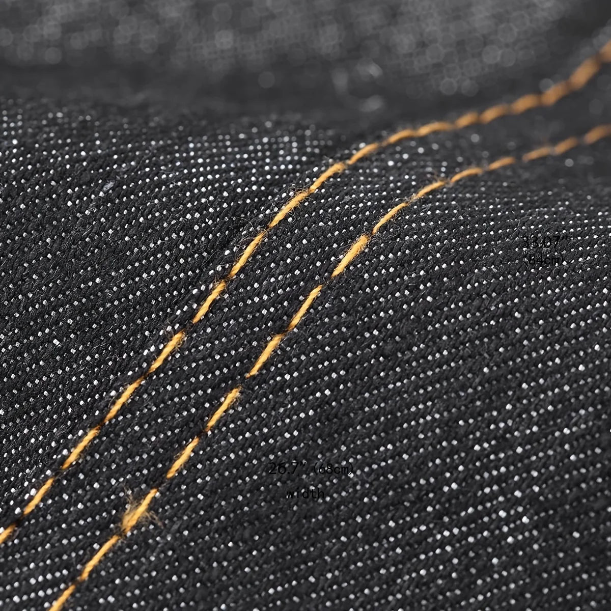 Close-up of dark denim fabric showing a visible orange stitching line on the material.