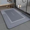 A rectangular gray bath mat with a non-slip rubber base and the word HOME printed on it, placed on a tiled floor.