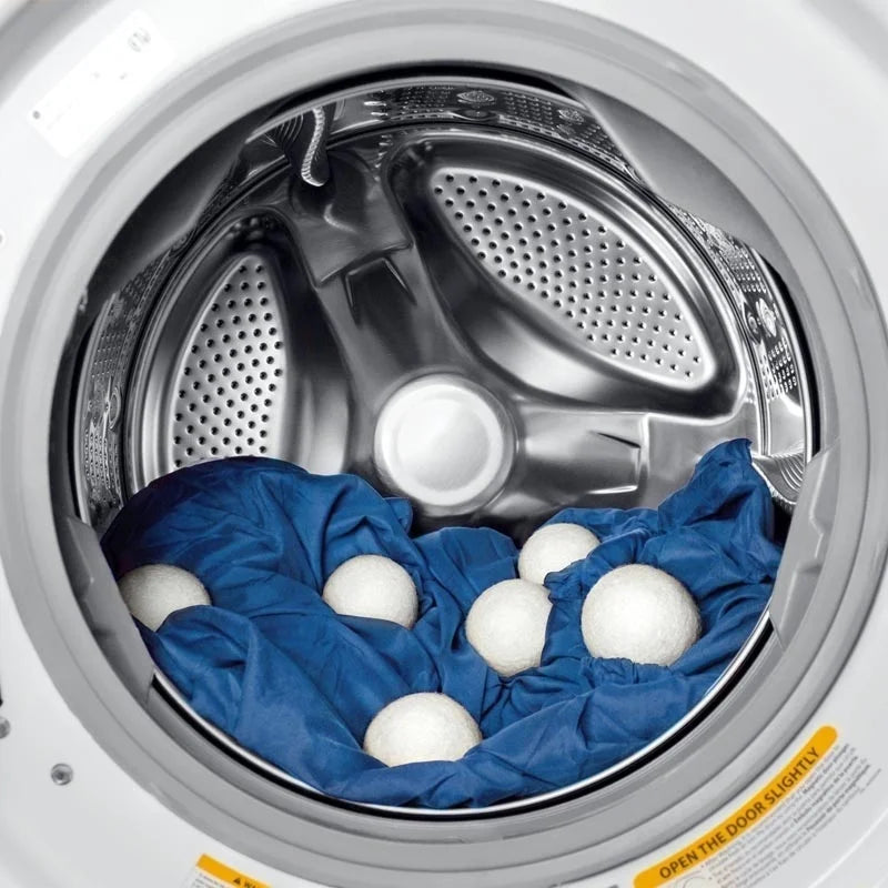 A set of three white natural wool dryer balls placed inside the drum of a washing machine.