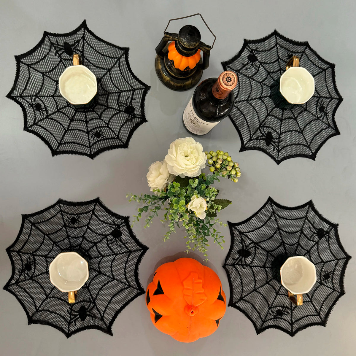 A set of disposable spider web placemats featuring white bowls and an orange pumpkin decoration.