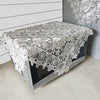 A silver lace tablecloth with an embroidered rose design is displayed on a table.