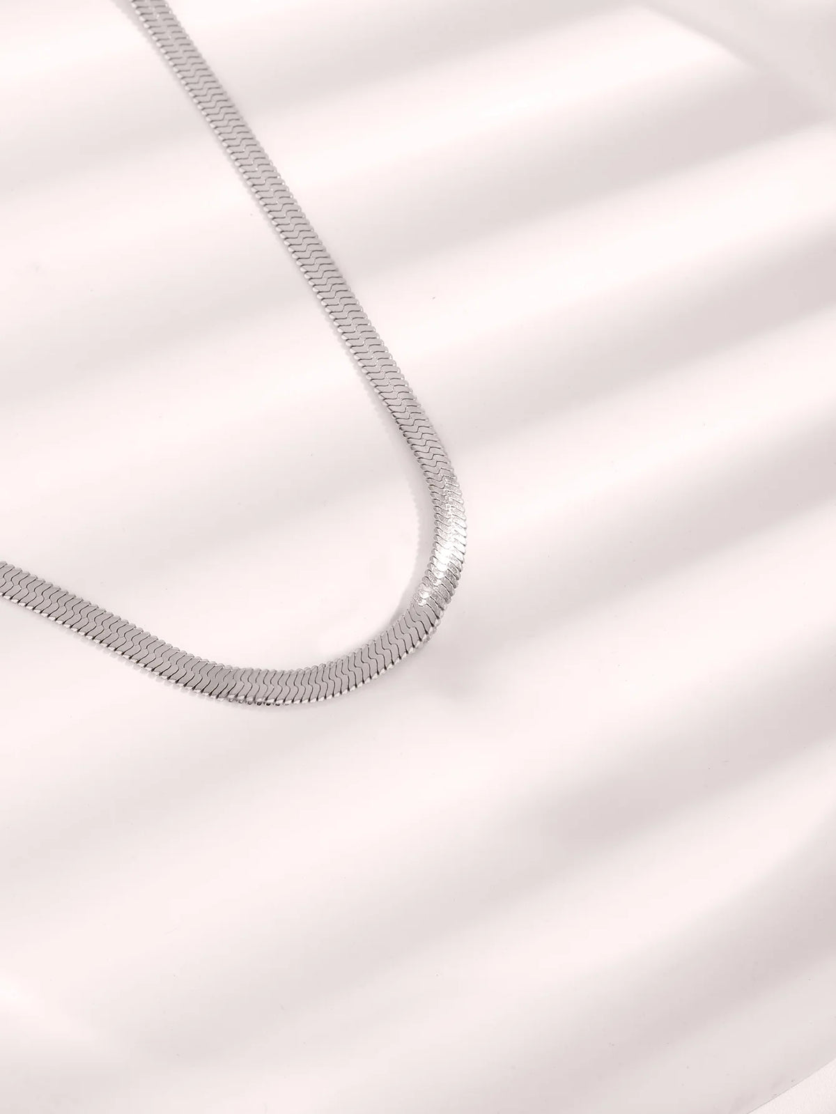 Collar de cadena de serpiente de acero inoxidable chapado en oro contra fondo blanco con sombras diagonales.