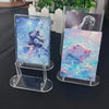 A clear acrylic display stand holding two photo cards featuring anime characters and a man's portrait.