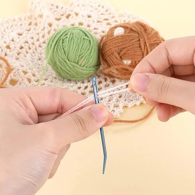 Hands are using bent tip tapestry needles to thread yarn for knitting or weaving.