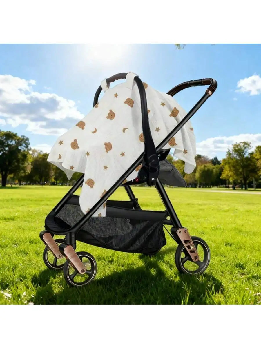 A white stroller cover with gold stars is shown on a black stroller frame outdoors in a sunny park.