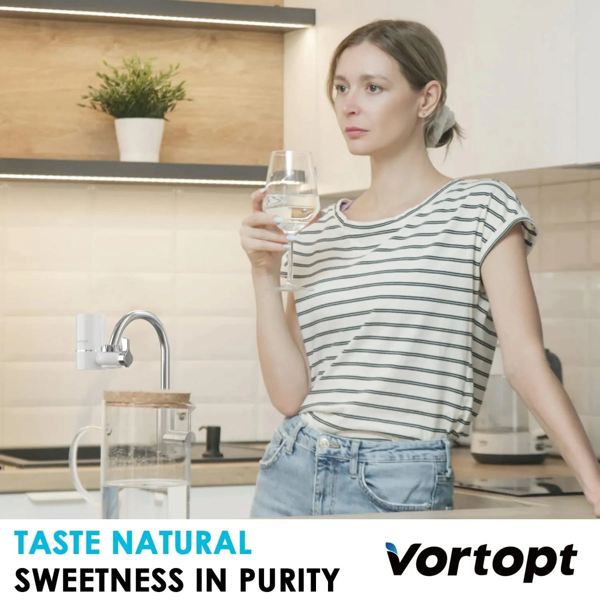 A woman is holding a glass of water near a kitchen faucet while standing in a modern kitchen setting.